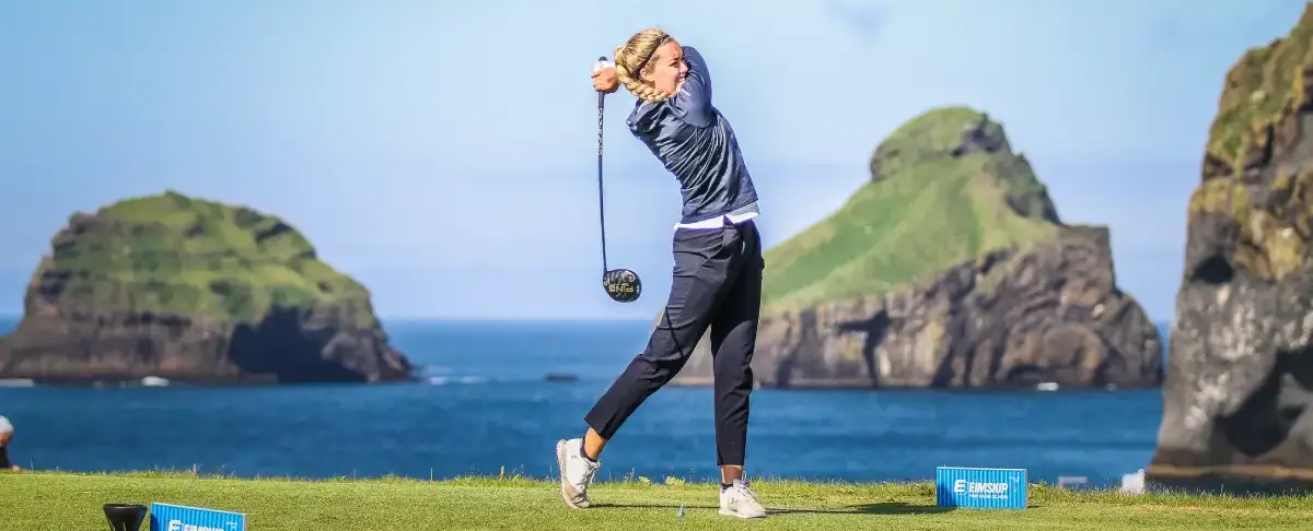 Woman teeing off at Vestmannaeyjar Golf Club with sea stacks in the background