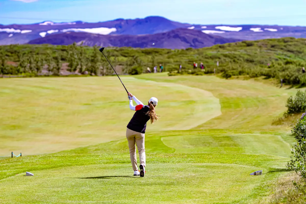 Golfer teeing off at Oddur Golf Club with mountains in the background