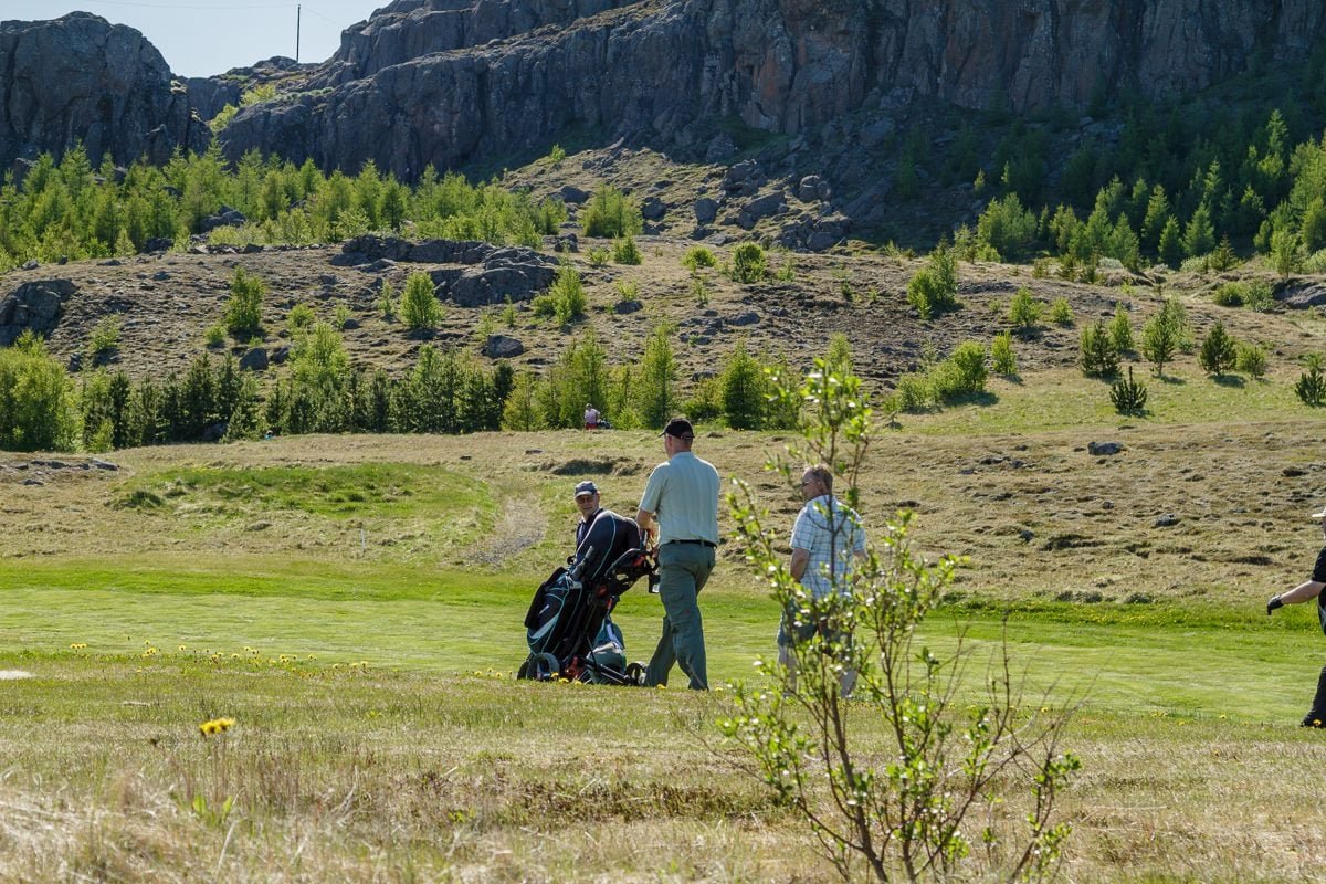 Golfers walking the fairway beneath a rocky outcrop at Ekkjufellsv&ouml;llur