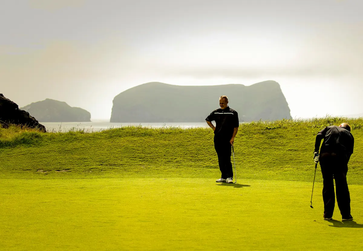 Golfers putting with the Elephant Rock sea stack in the background