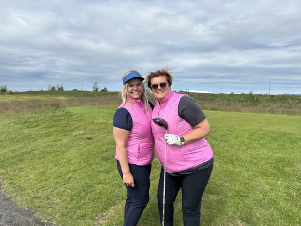 Two golfers in pink vests smiling together on a golf course