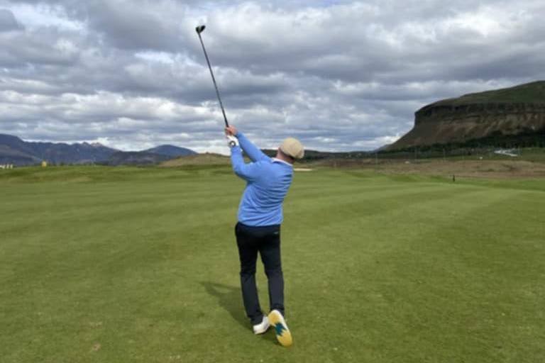 Golfer following through on a swing with mountains and cliffs in the background